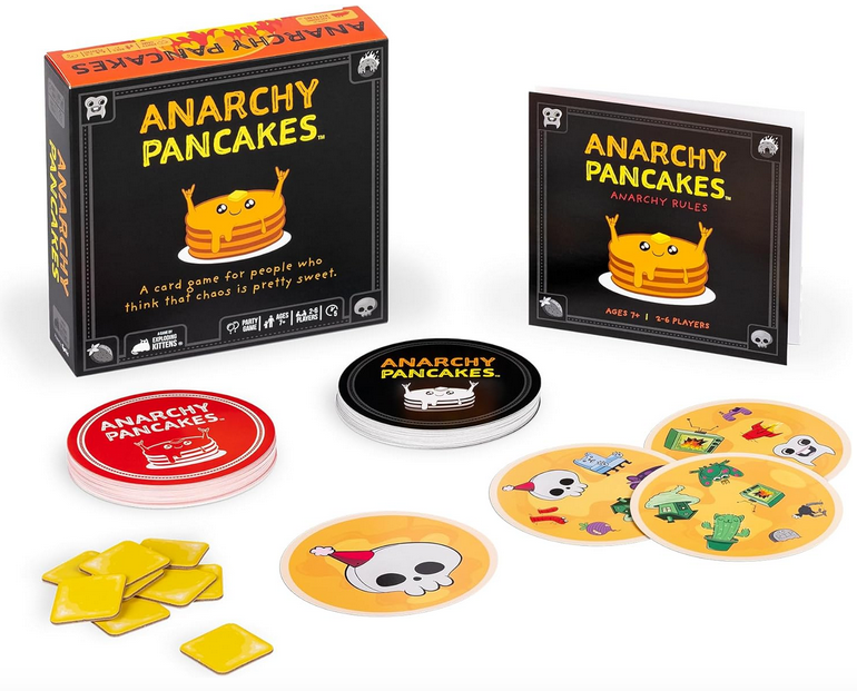 The Anarchy Pancakes game box standing up in the background with the cards set up for game play. There is a stack of red circular cards, black circular cards and square yellow tokens. 