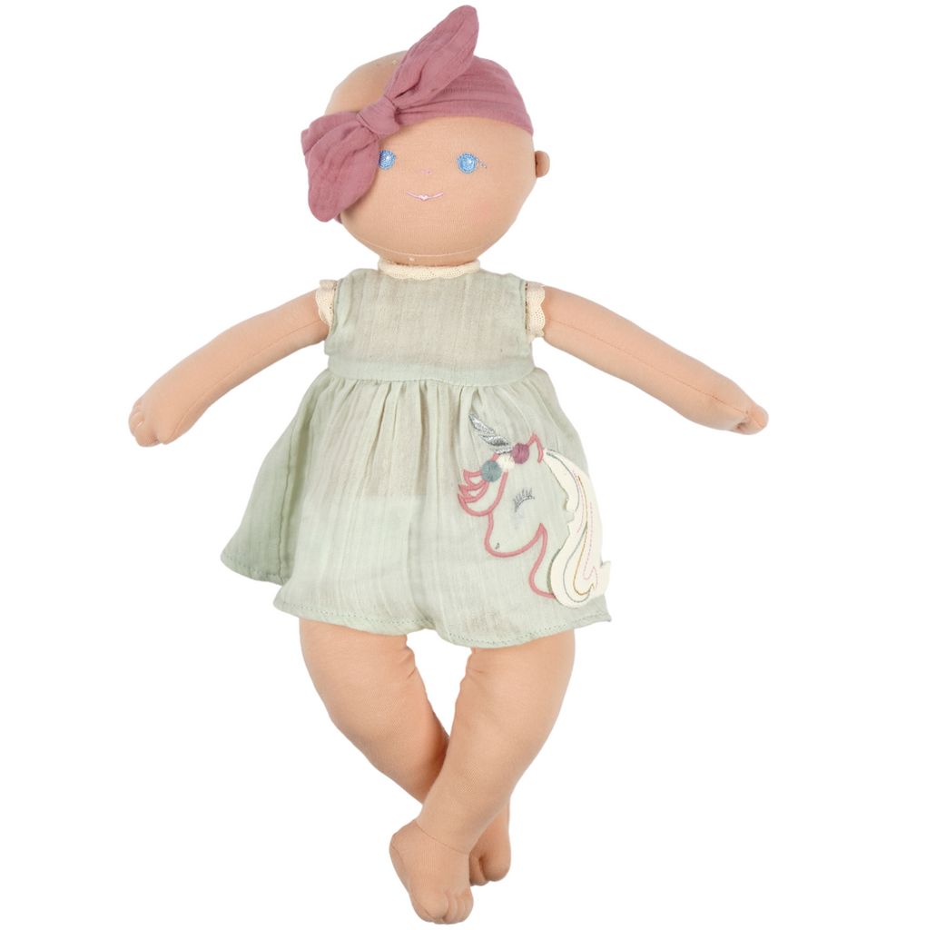 Baby Kaia soft doll wearing a light blue dress with a unicorn embroidered on the front of it. She also is wearing a pink headband.