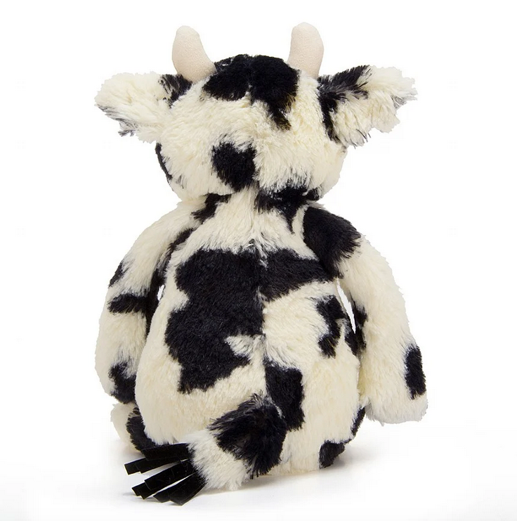 Bashful Cow viewed from the back. It has black and white fur all over, white horns and a black tasseled tail. 