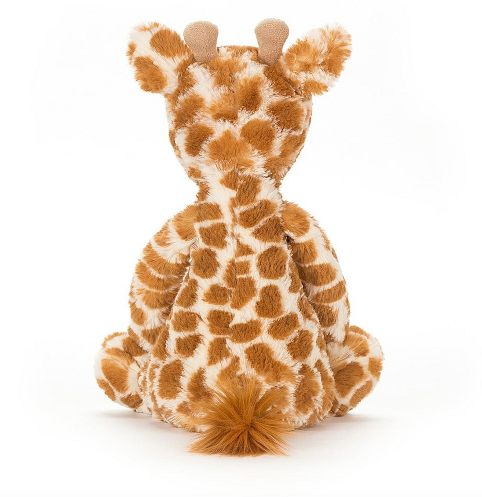 Bashful Giraffe plush viewed from the back. With fuzzy orange and tan spotted fur and fluffy tail.