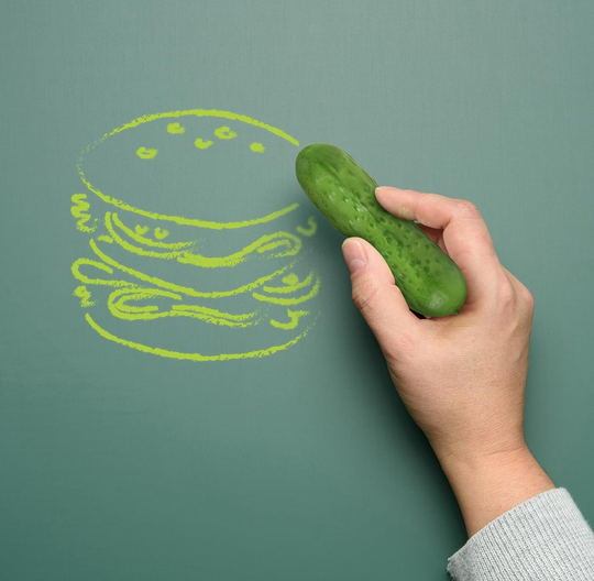A drawing of a hamburger on a green chalkboard made with a hand holding the Big Dill SIdewalk Chalk. 