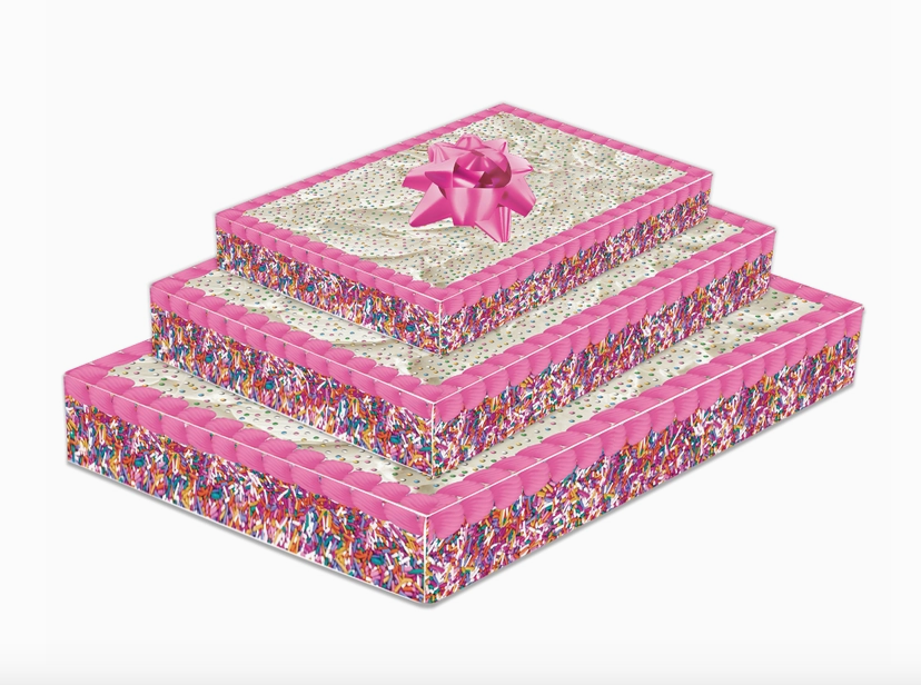 Three gift boxes layered to look like a big cake with white icing and colorful confetti. Topped with a pink bow.