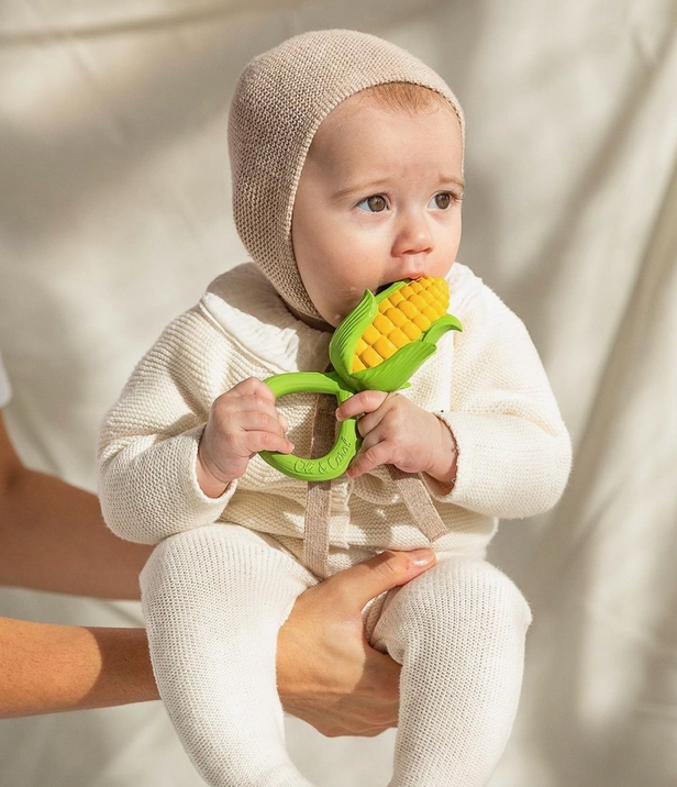 A little baby chewing on the corn rattle toy while being held. 