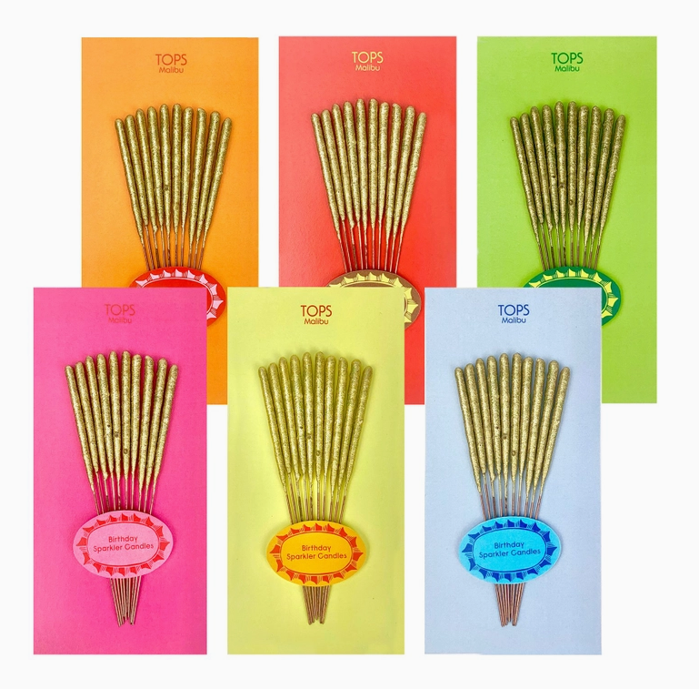 Mini gold sparklers packaged on assorted colored backing cards in clear cellophane. There is orange, red, green, pink, yellow and blue. 