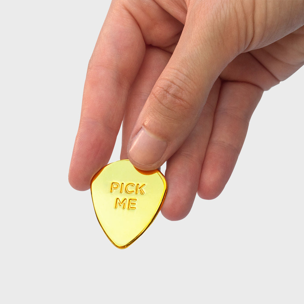 The gold guitar pick lucky charm being held. The front side is engraved with "Pick Me"