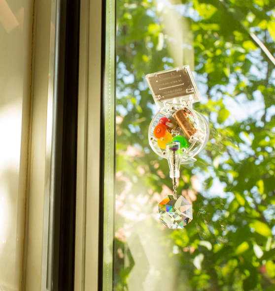 The clear rainbow maker with solar panel at the top and crystal at the bottom attached to a window. 