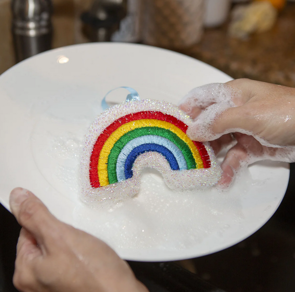 The white rainbow scrubber sponge beign used to wash a white plate. 