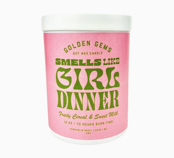 Pink jar with green lettering that reads " Smells Like Girl Dinner" "Fruity Cereal & Sweet Milk".  A white top covers the jar. 