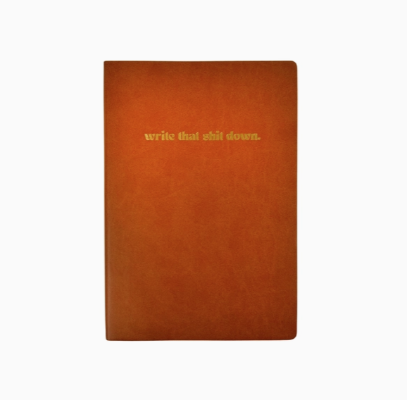 Brown vegan leather bound journal with "write that shit down" in gold foiled letters on the cover.