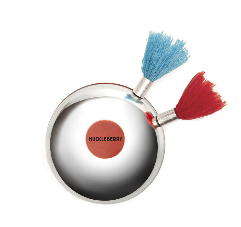 A silver bell with two magnetic darts attached. One dart has a red fringe fly and the other has a blue fringe fly. A red sticker with the word Huckleberry is the bullseye on the bell. 