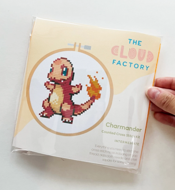 The Charmander Cross Stitch kit in it's package with an illustration of the included pattern of Charmander with flames on it's tail