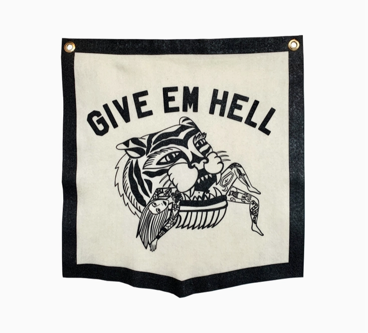 White felt pennant with black border and lettering that reads "Give em hell" with a tiger outlined that has a tattooed woman in it's mouth. 