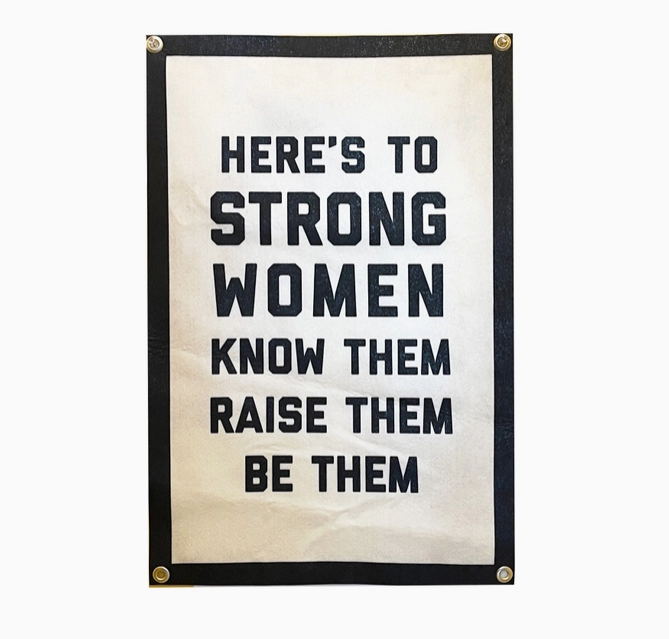 Rectangle felt banner with off white background and black border and lettering that reads "Here's to strong women, know them, raise them, be them. "