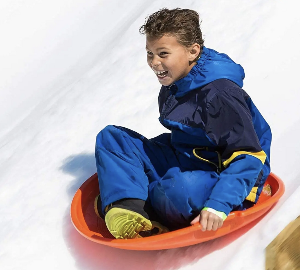 Kid sledding down a snowy hill in a red saucer sled.