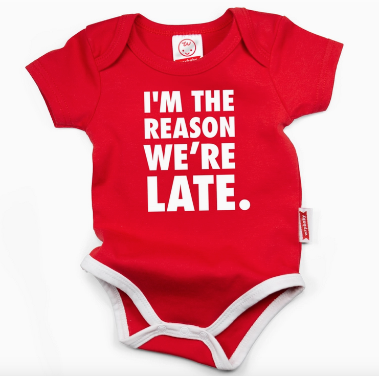 Red 3 snap baby onesie with white trim and white block lettering that reads "I'm The Reason We're Late"