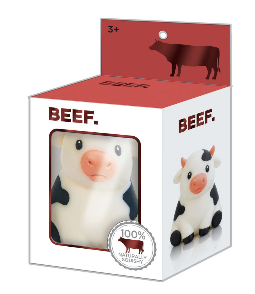The 100% Naturally Squishy Beef stress toy shaped like a black and white cow, packaged in a white box with a window at the front that shows the cute cow inside. 