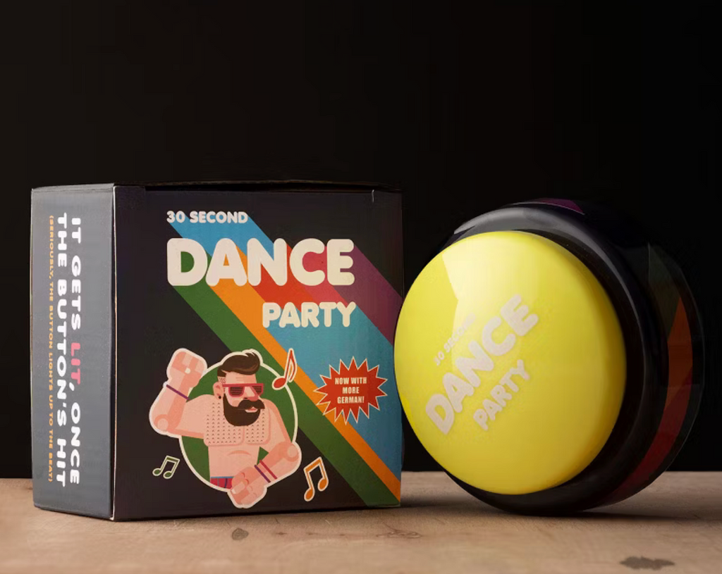 The 30 Second Dance Party button resting against the box it comes packaged in which is black with green, yellow, blue and red stripes along side an illustrated picture of a buff dude surrounded by music notes.