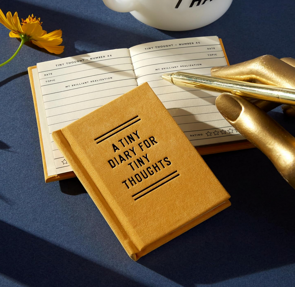 "A Tiny Diary For Tiny Thoughts " being written in with a gold pen to show scale of it's tinyness.