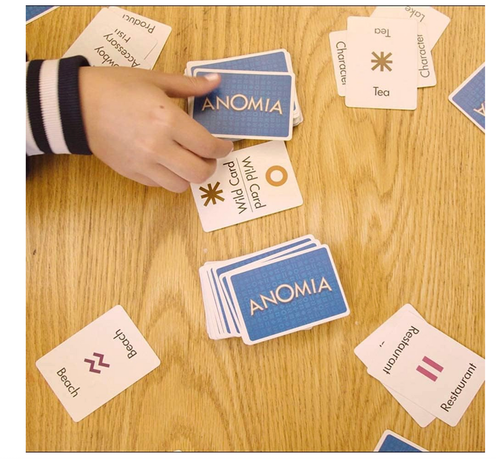 Hand playing a card game with 'ANOMIA' cards on a wooden table