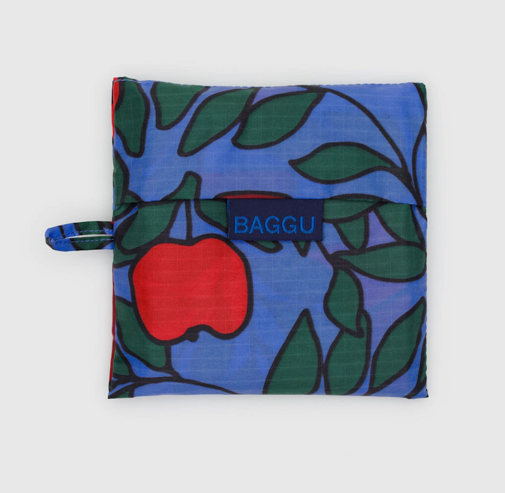 Baggu standard bag folded into it's flat storage pouch with an apple tree pattern on a bright blue background. 