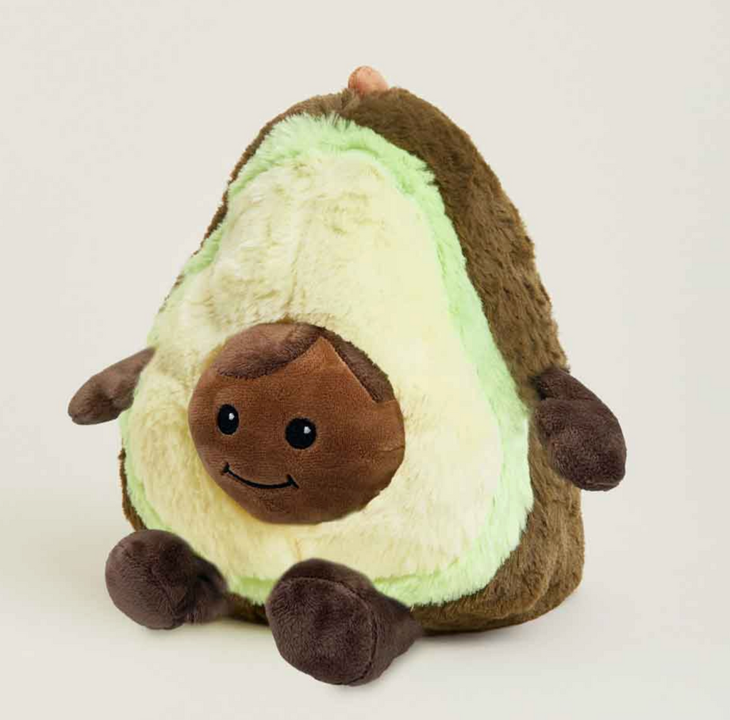 Warmies Avocado plush with a soft fuzzy texture, featuring a brown outer skin, a pale green inner flesh, a brown seed face with embroidered eyes and a smile, and small dark brown arms and legs. 