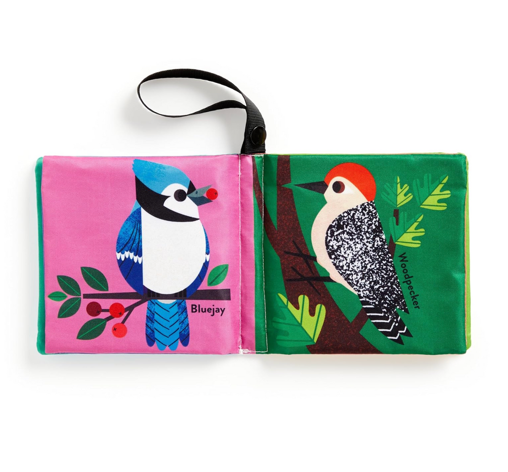 The Baby Birder Crinkle Fabric Stroller Book open to show a Bluejay on one page and a Woodpecker on the other. Each page has bright contrasting colors. The loop used to attach to the stroller or car seat is also visible. 