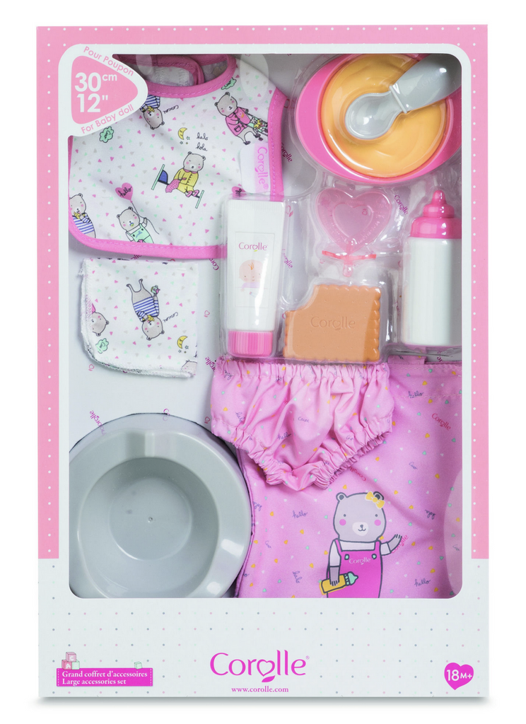 The Baby Doll Accessories Set in pink packaged in a see through box to show the tote bag, diaper cover, feeding set and bib that are all included in the set. 