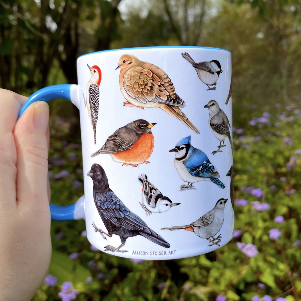 A white ceramic mug with light blue handle and interior that has illustrations of common back yard birds all over it. 
