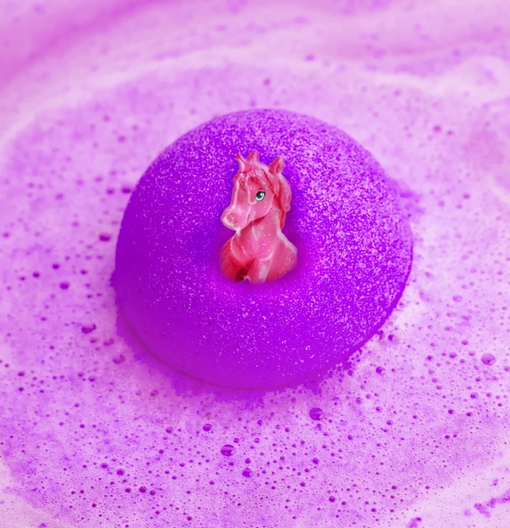 A pink unicorn emerging from a purple bath bomb floating in purple water. 