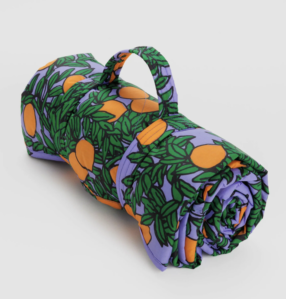 Baggu puffy picnic blanket in orange tree print on periwinkle background rolled up to carry. 