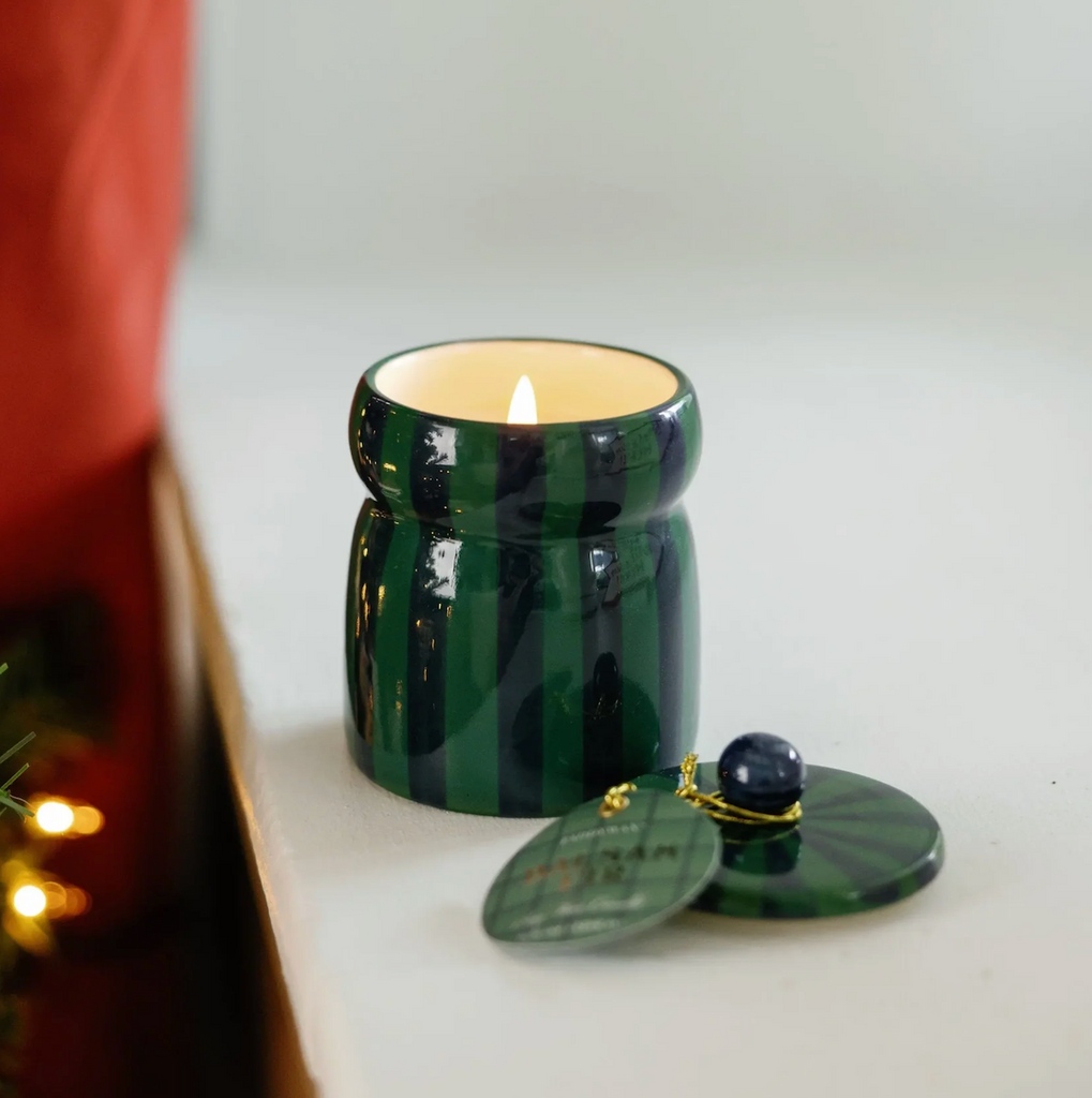Green striped candle in a decorative jar with a lit candle inside.