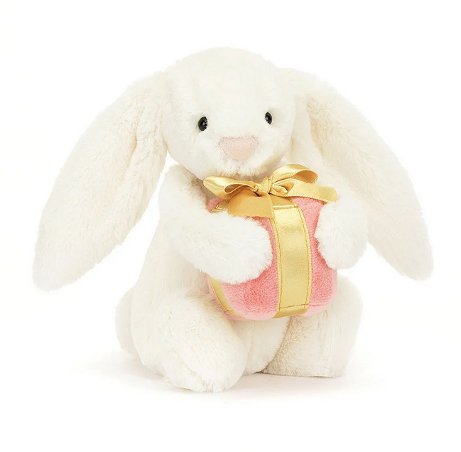 Cream colored plush bunny holding a pink plush present wrapped in gold satin ribbon.