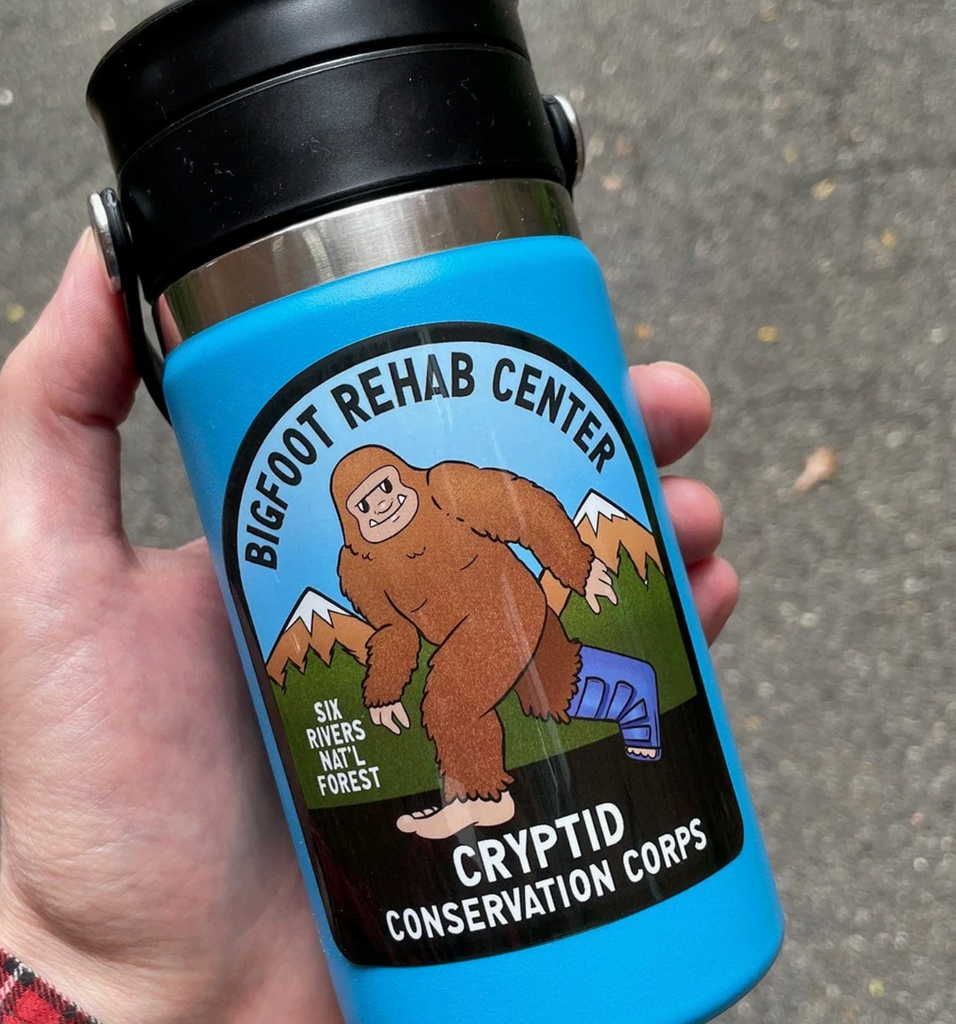 Sticker with illustration of a brown bigfoot walking with his right foot in a boot. The sticker reads "Bigfoot Rehab Center, Cryptid Conservation Corps" on a water bottle. 