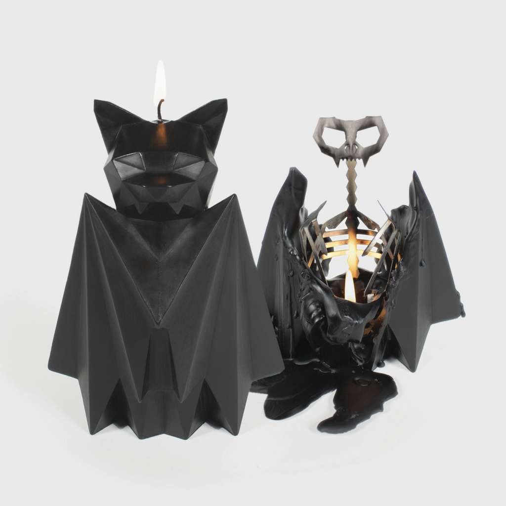 Black bat shaped candle burning down to reveal a metal skeleton inside on a white background.