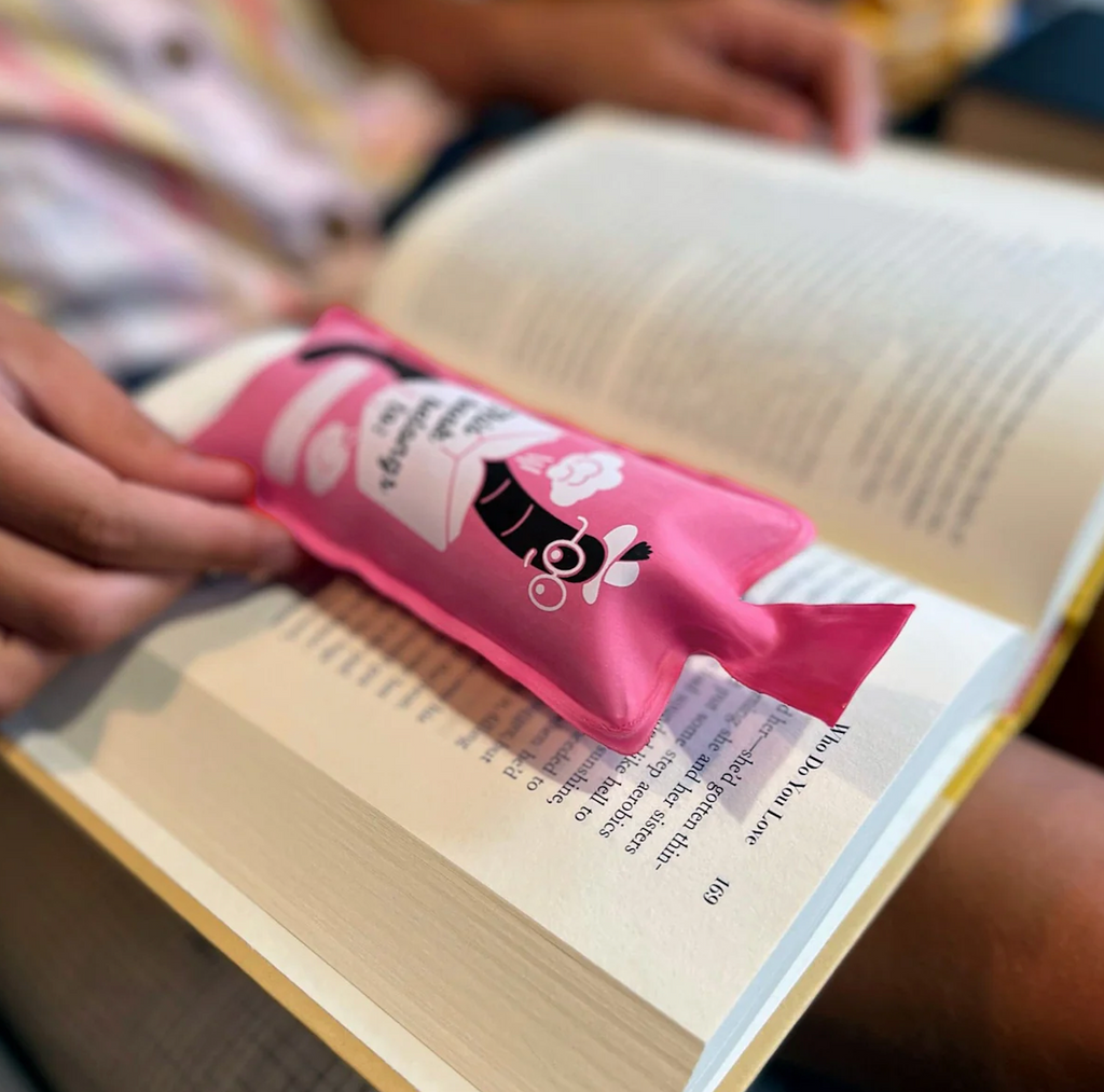 Inflated pink "Bookie Cushion" bookmark resting in an open book. 