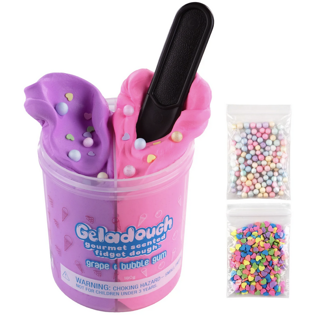 Clear container filled with purple and pink scented fidget dough. The purple is grape scented and the pink is bubblegum scented. There are two bags containing mix ins for the dough. One bag has pastel colored beads ans the other has brightly colored heart shaped confetti. 