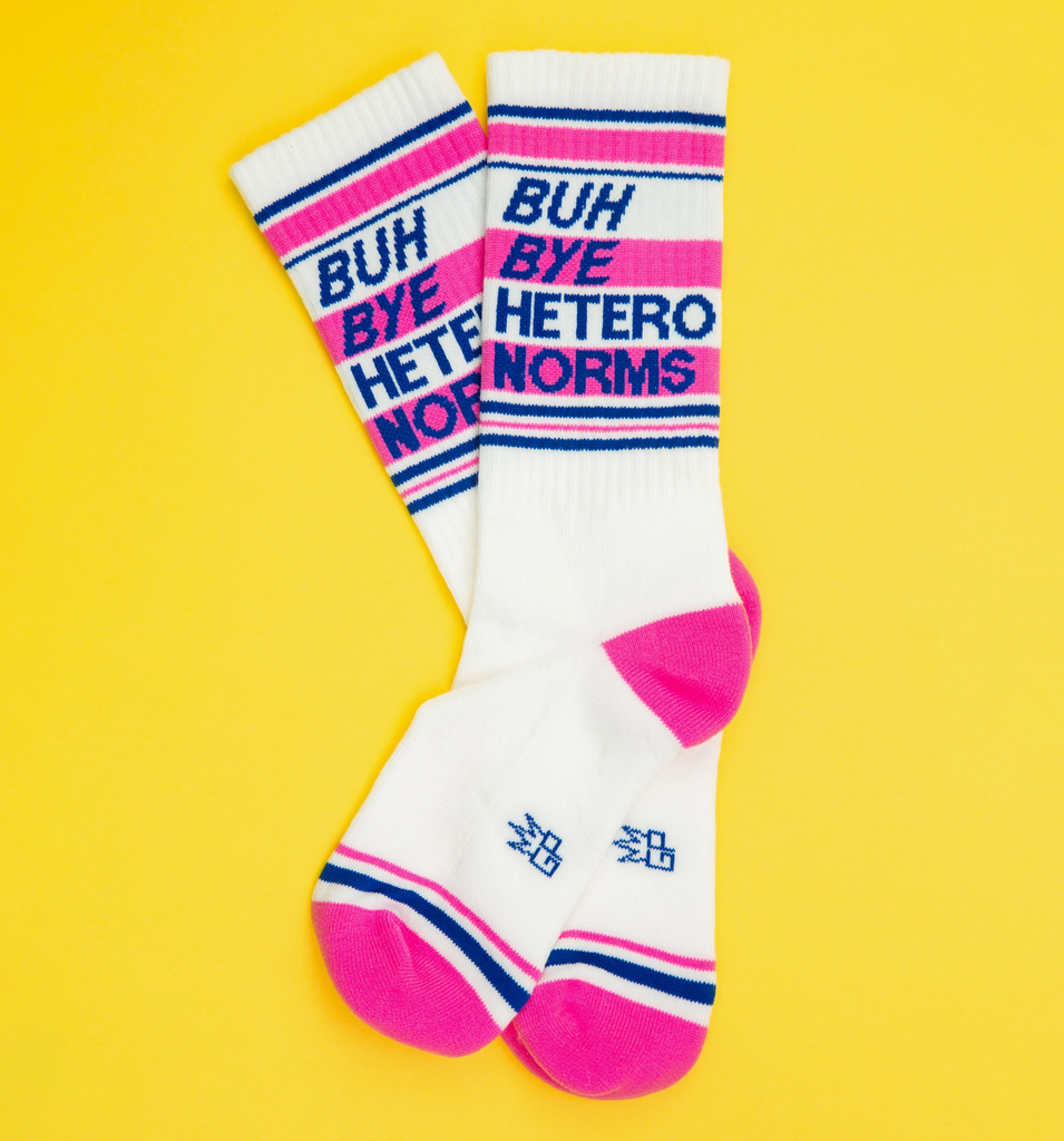 White tube socks with hot pink and blue stripes that read " Buh Bye Hetero Norms" in blue letters. 