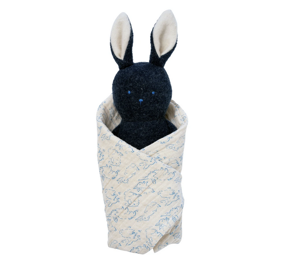Dark grey plush bunny rattle swaddled in a cotton gauze burp cloth that is an off white with blue bunny pattern. 