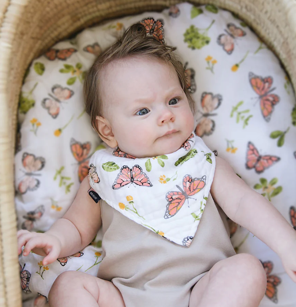 A baby in a bassinet wearing the Butterfly Muslin bib.