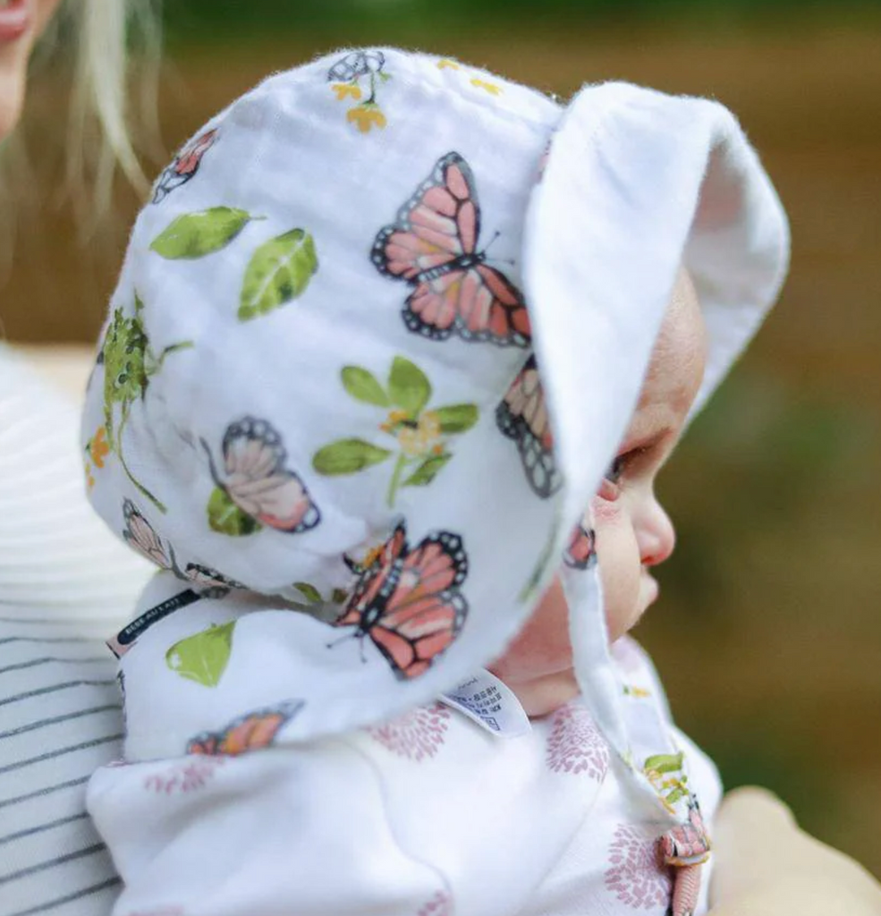 A baby wearing the Butterfly Muslin Sun Hat with the front brim turned up.