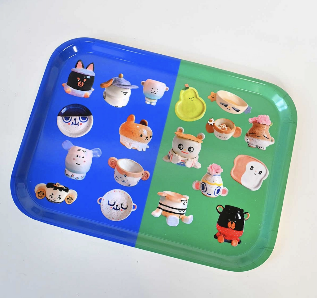 A picture of the Ceramic Party Catch All Tray which has a two tone colorway of green and blue with images of adorable ceramic creations like cups, plates and planters all of cute, kawaii animals and creatures. 