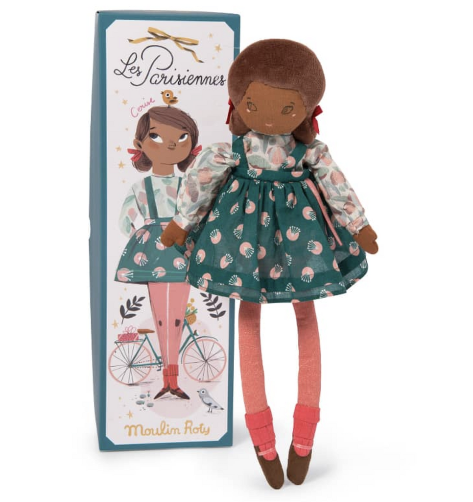 Cerise a plush doll from The Parisiennes Collection. Wearing a flouncy, teal floral dress, and standing in front of the illustrated gift box she comes packaged in. 