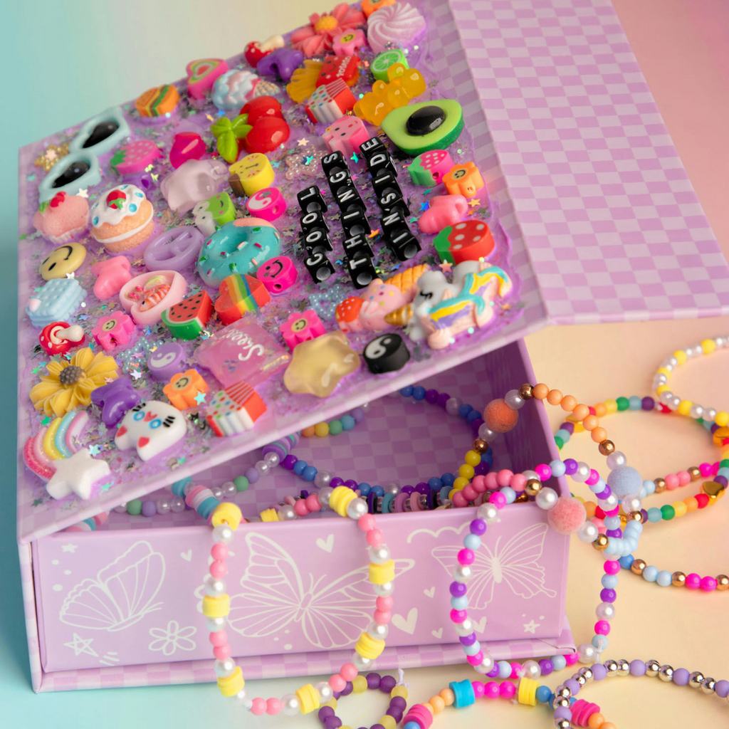 The lid of the Chaotic Crafts DIY Jewelry Box opened to show beaded braclets spilling out while teh lid itself is decorated with all sorts of cute and sweet charms. 