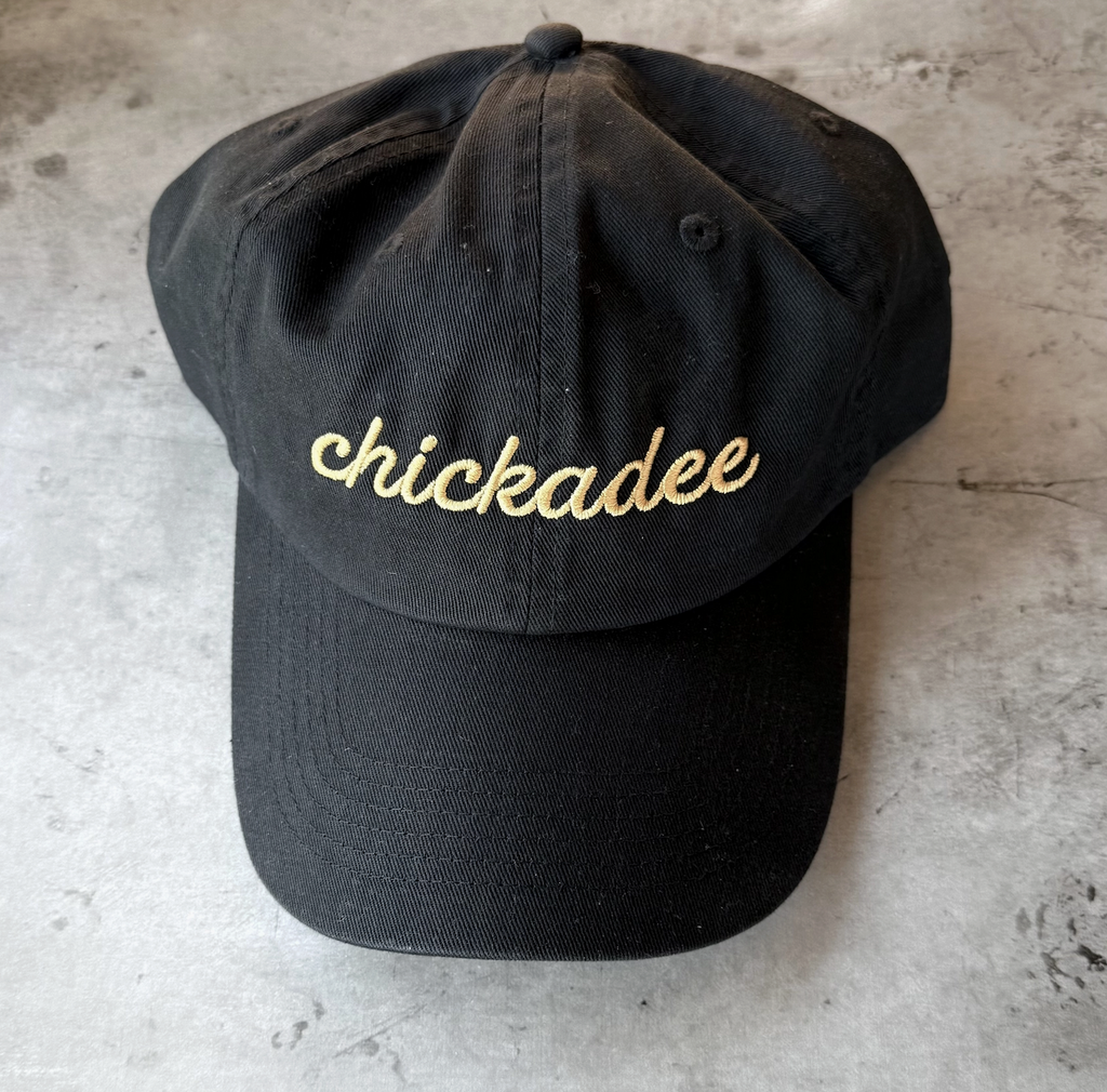 A black ball cap with yellow embroidery that says "Chickadee" 