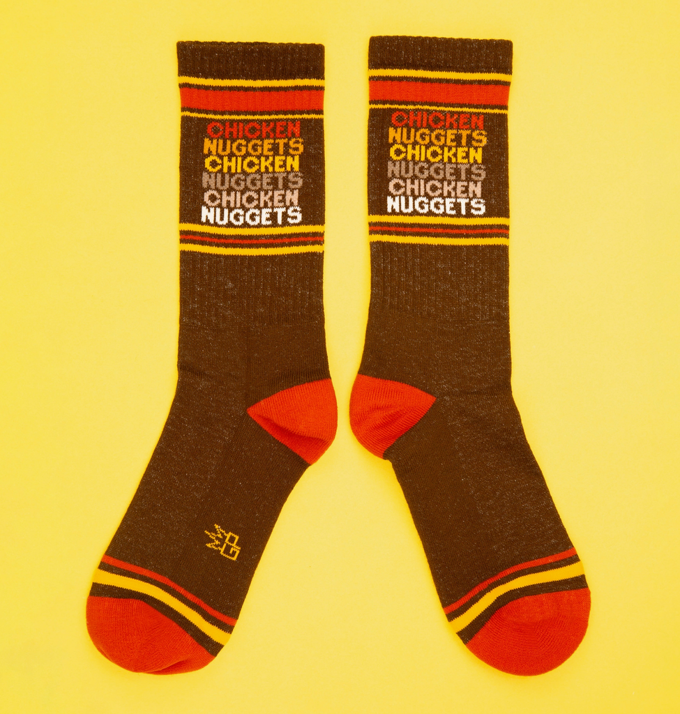 A pair of dark brown tube socks with yellow and orange stripes that read "Chicken Nuggets" in a repeating pattern.