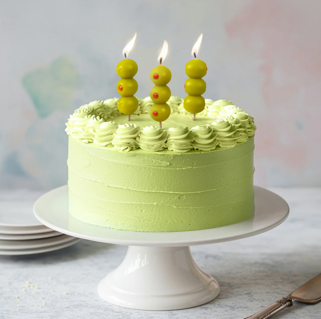 Green cake with Cocktail Party green olive candles on a white stand. 