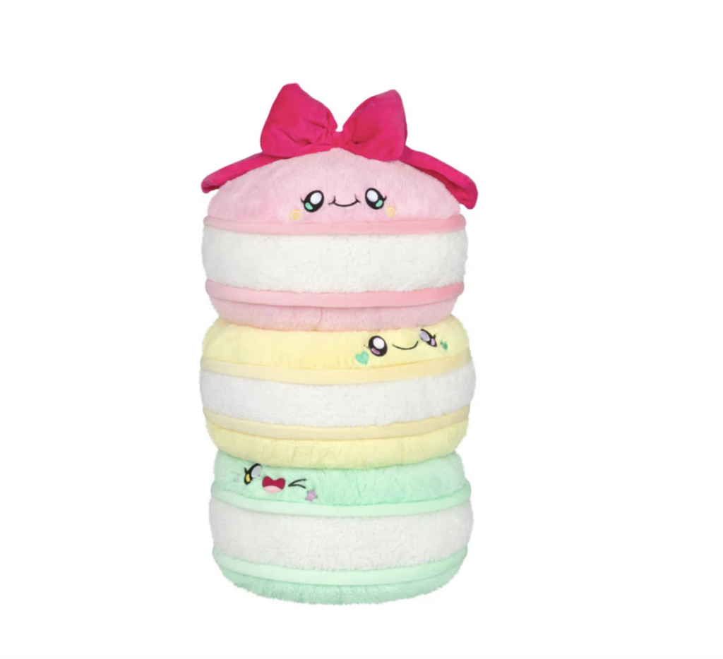 Three plush, pastel colored, stacked macarons with smiling faces and pink bow on the top. 