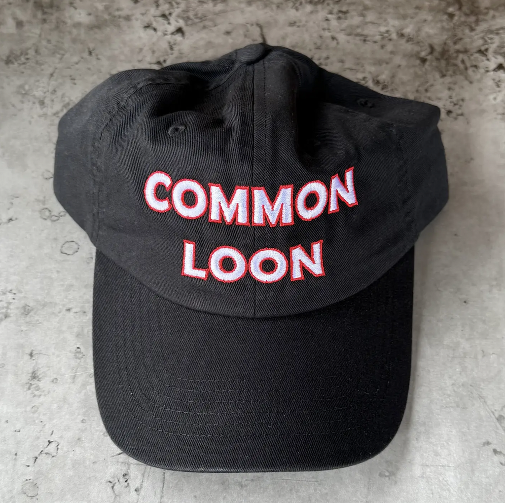 Black ball cap with "Common Loon" written on the front in white letters bordered by red. 