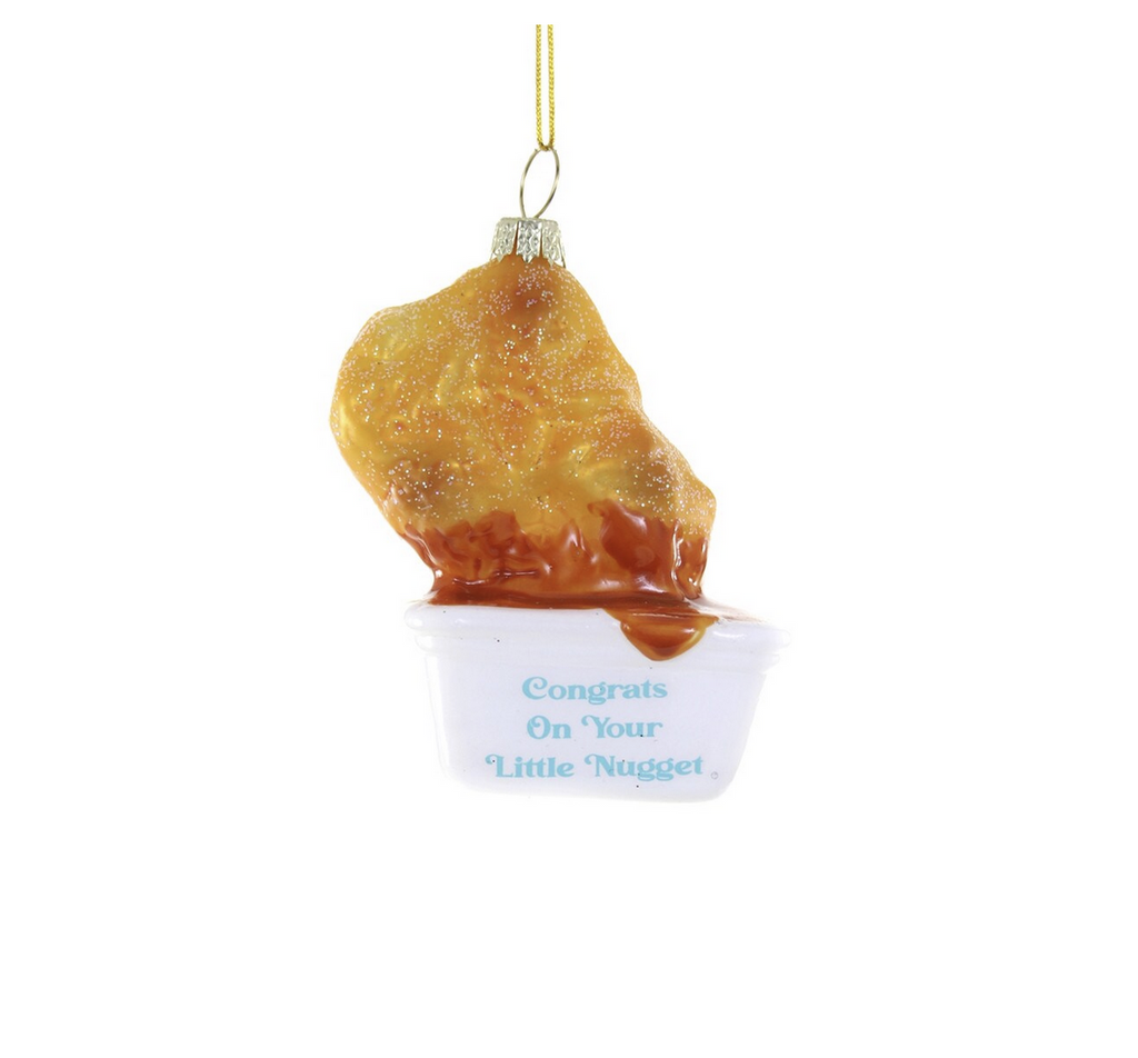 Glass chicken nugget being dunked into a sauce container glass ornament. Text on sauce container reads "Congrats on your little nugget"