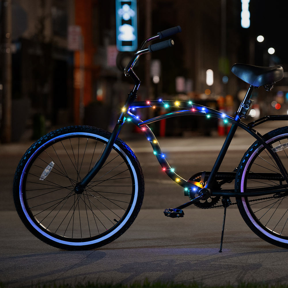 A bike on the street at night. The bike has the Cosmic Brightz Rainbow lights wrapped around the frame. 
